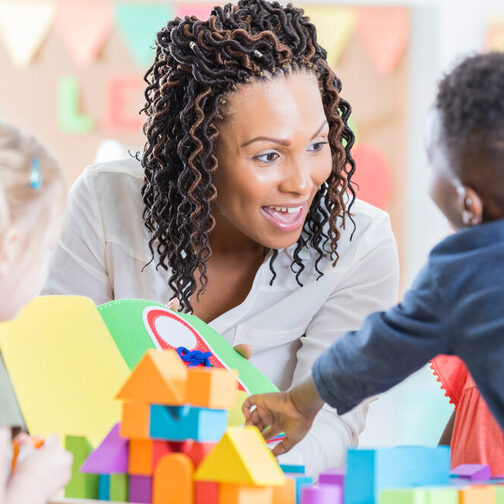 Eine lachende Erzieherin spielt mit Vorschulkindern