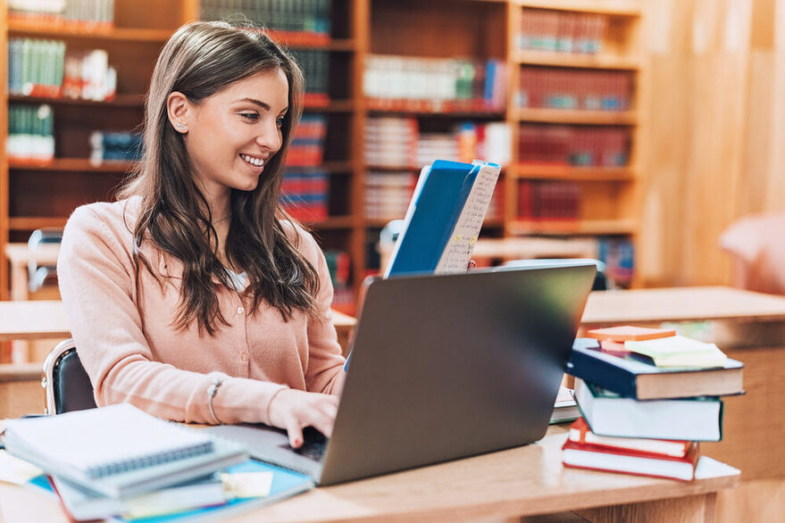 Eine junge Frau mit dunklen Haaren sitzt an einem Schreibtisch und arbeitet an einem Laptop