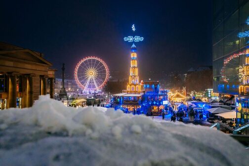Nächtlicher Blick auf den Schlossplatz in Stuttgart mit leuchtender Pyramide und Riesenrad.