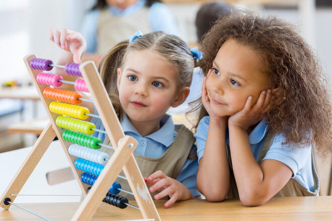 Zwei Mädchen spielen an einer Kinder-Rechenmaschine.